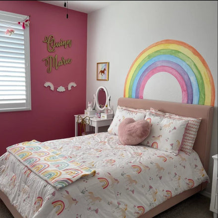 Pastel watercolor rainbow wall decal used as a headboard above a pink bed in a girl's room with pink walls