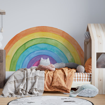 Colorful watercolor rainbow wall decal placed as a headboard behind a wooden house-shaped bed frame
