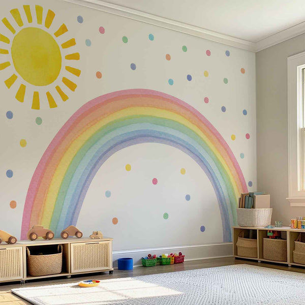 Large watercolor wall decal featuring a pastel rainbow arch, a large yellow sun, and colorful polka dots in a bright, modern nursery and playroom.