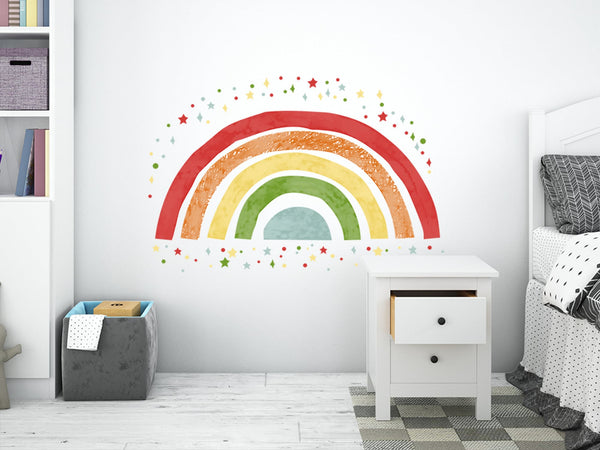 Watercolor style rainbow wall decal in red, yellow, and green with scattered star stickers on a white wall in a child's bedroom